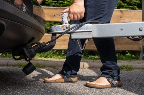 woman's hand checks the fixation of the trailer closed hitch lock handle on the towing ball towbar of the car closeup, the safety of driving with a trailer on the road